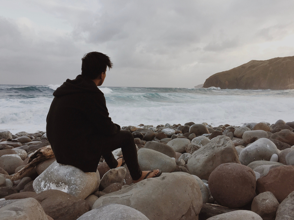 Young Man Sitting On Rocks By The Sea 